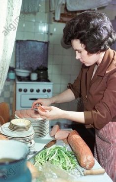 a woman in an apron is making food on a counter top with stacks of plates and pans