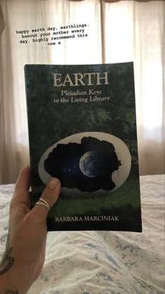 a person holding up a book in their hand with the earth on it's cover