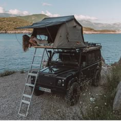 a woman standing on top of a ladder next to a vehicle with a tent over it