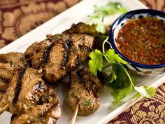 grilled meat on skewers with dipping sauce and garnished cilantro