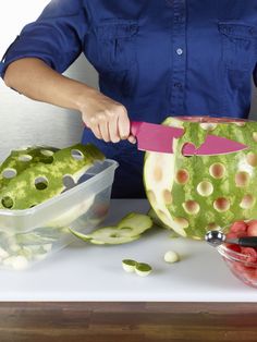 a woman cutting up a watermelon with a knife and bowl of fruit in front of her