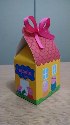 a peppa pig house shaped box with a pink bow on the top, sitting on a table