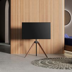 a flat screen tv sitting on top of a wooden tripod in front of a bed