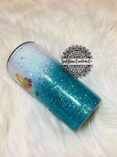 a blue and green glittered cup sitting on top of a white fur covered floor