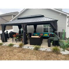 a patio covered in black curtains and furniture next to a white house with grey siding