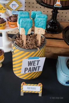 desserts are displayed in buckets with signs on the table and cupcakes behind them