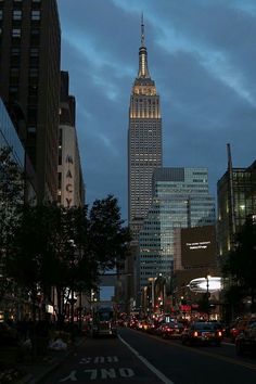 the empire building is lit up at night in new york city, with cars driving down the street