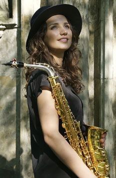 a woman holding a saxophone in her right hand and wearing a hat on top of her head