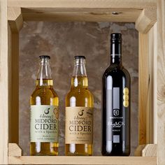 three bottles of cider sit in a wooden box on a shelf next to each other