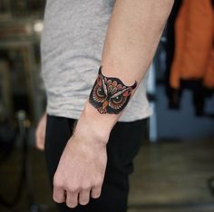 an owl tattoo on the left wrist is shown in black and red colors, with orange accents