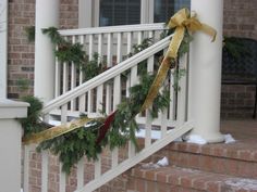 christmas garland tied to the banisters on a front porch with gold ribbon and bows