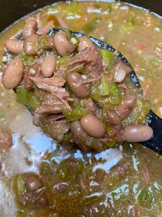 a ladle full of beans and meat in a pot with broth on it