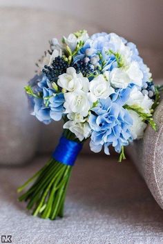 a bouquet of blue and white flowers is sitting on the arm of a couch in front of a chair