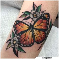 an orange butterfly with flowers on it's arm, sitting on top of a woman's leg