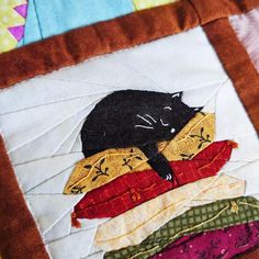 a black cat sitting on top of pillows in a patchwork quilted square pattern