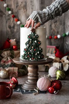 someone decorating a christmas tree cake on top of a wooden stand with ornaments around it