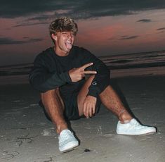 a young man sitting on the beach at night with his legs crossed and feet crossed