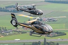 two black and yellow helicopter flying over green fields