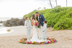 a bride and groom are standing on the beach with their two children in front of them