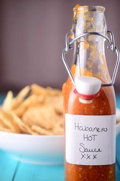 a bottle of hot sauce next to some chips on a blue table with a white plate