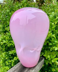 a pink glass sculpture sitting on top of a wooden bench in front of green bushes