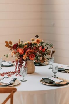 an arrangement of flowers in a vase on top of a white table cloth with place settings