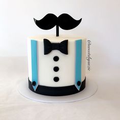 a white cake with blue trim and a black bow tie on top, topped with a fondant moustache