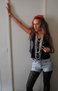 a woman in black shirt and jean shorts standing next to a wall with her hand up