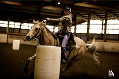 a man riding on the back of a brown horse next to a white barrel in an indoor arena