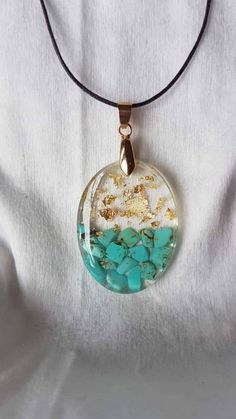 a glass pendant with gold glitter and turquoise stones in it on a black cord necklace