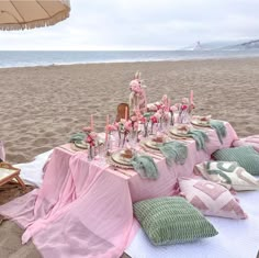 a table set up on the beach with pink and green linens for an outdoor dinner