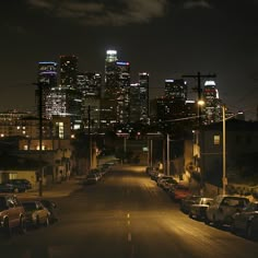 the city skyline is lit up at night, with cars parked on the side of the street