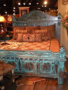 an old bed with pillows and blankets on it in a store display area, surrounded by other antique furniture