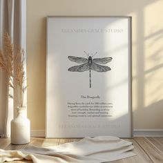 a poster with a dragonfly on it next to a vase and some dried grass