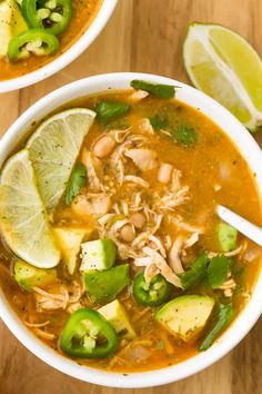 two bowls of chicken tortilla soup with limes, avocado and cilantro