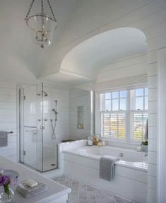 a large white bathroom with an arched ceiling and chandelier above the bathtub