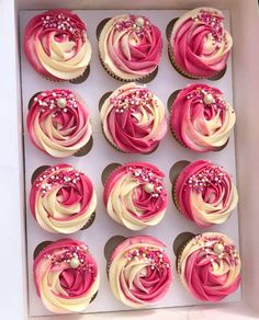 twelve cupcakes with pink and white frosting in a box on a table