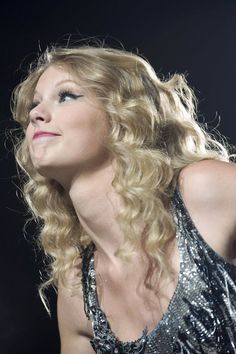 a woman with long blonde hair wearing a black and silver dress looking up at the sky