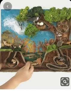 a person is holding up a paper cutout with animals and trees on the bottom