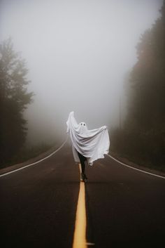 a person is walking down the road with a white sheet on their head and there are trees in the background