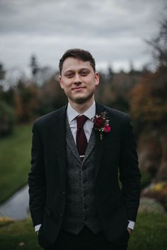 a man wearing a suit and tie standing in front of a pond with flowers on it