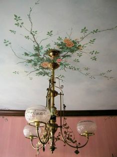 a chandelier hanging from a ceiling with flowers painted on the wall behind it