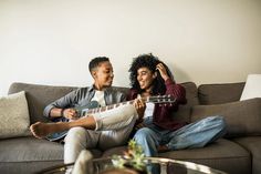 a man and woman are sitting on a couch playing the ukulele guitar together