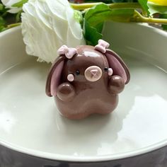 a small brown elephant figurine sitting on top of a white plate next to flowers