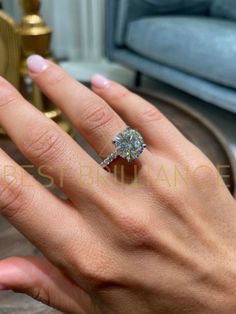 a woman's hand with a diamond ring on top of her finger, in front of a couch