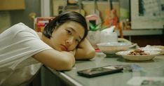 a young man leaning his head on a counter in front of a bowl of food