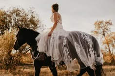 a woman riding on the back of a black horse wearing a white dress and veil