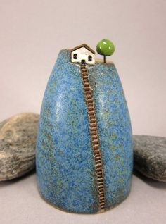 there is a small blue vase with a green ball on top and a house in the middle