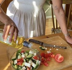 a woman is preparing a salad with tomatoes and cucumbers on a cutting board