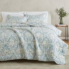 a bed with blue and white bedspread in a room next to a plant